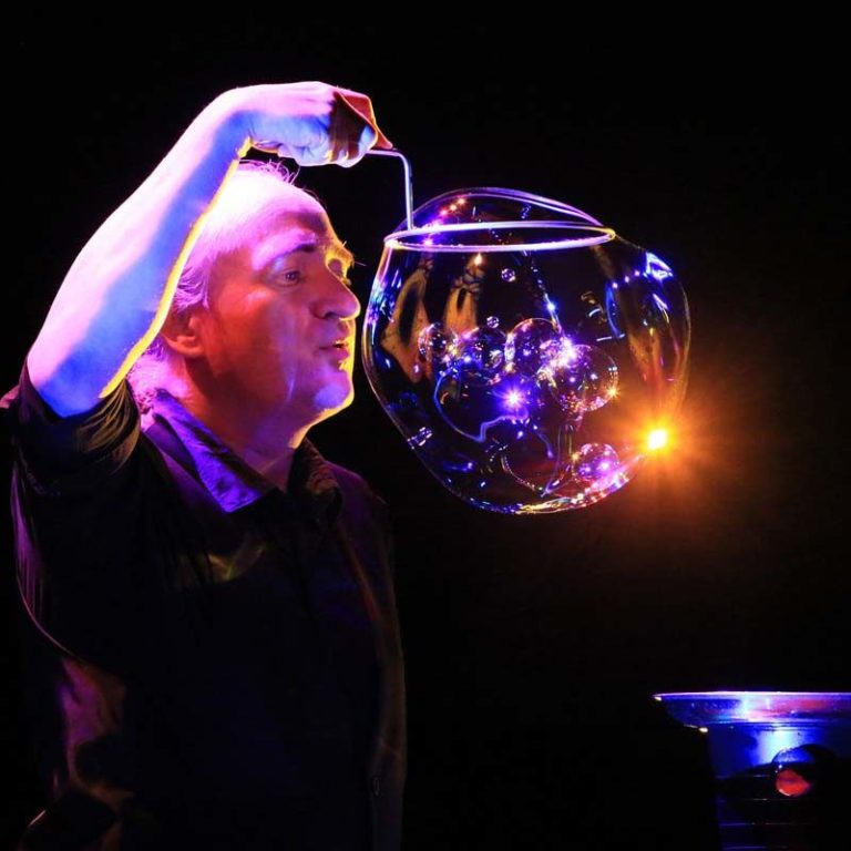 De Bubbelstelsel — een reuze bellenblaas die vele kleine zeepbellen bevat. Een man vormt een grote zeepbel die vele kleine zeepbellen bevat, en concentreert zich erop.