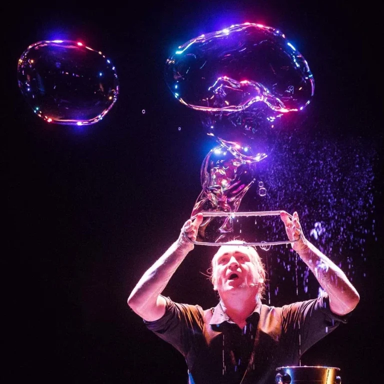 Stephan Masur Bubble Show in Nederland Een bellenblaaskunstenaar maakt een gigantische zeepbel met een lus onder kleurrijk licht.