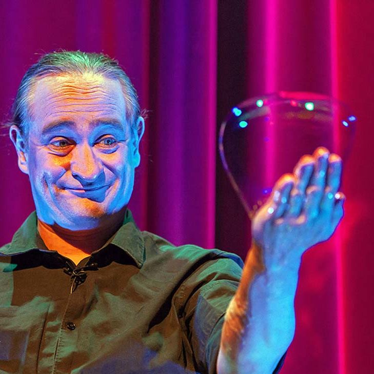 Handzeepbel - zeepbellenshow van Stephan Masur in Nederland Een man houdt een grote zeepbel in zijn hand tegen een kleurrijke achtergrond.